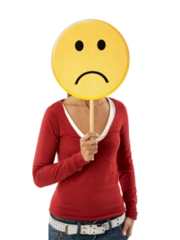 Woman holding a frowning face mask in front of her face.