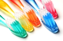 Photo of five toothbrushes, each a different color, green, yellow, orange, blue and red.
